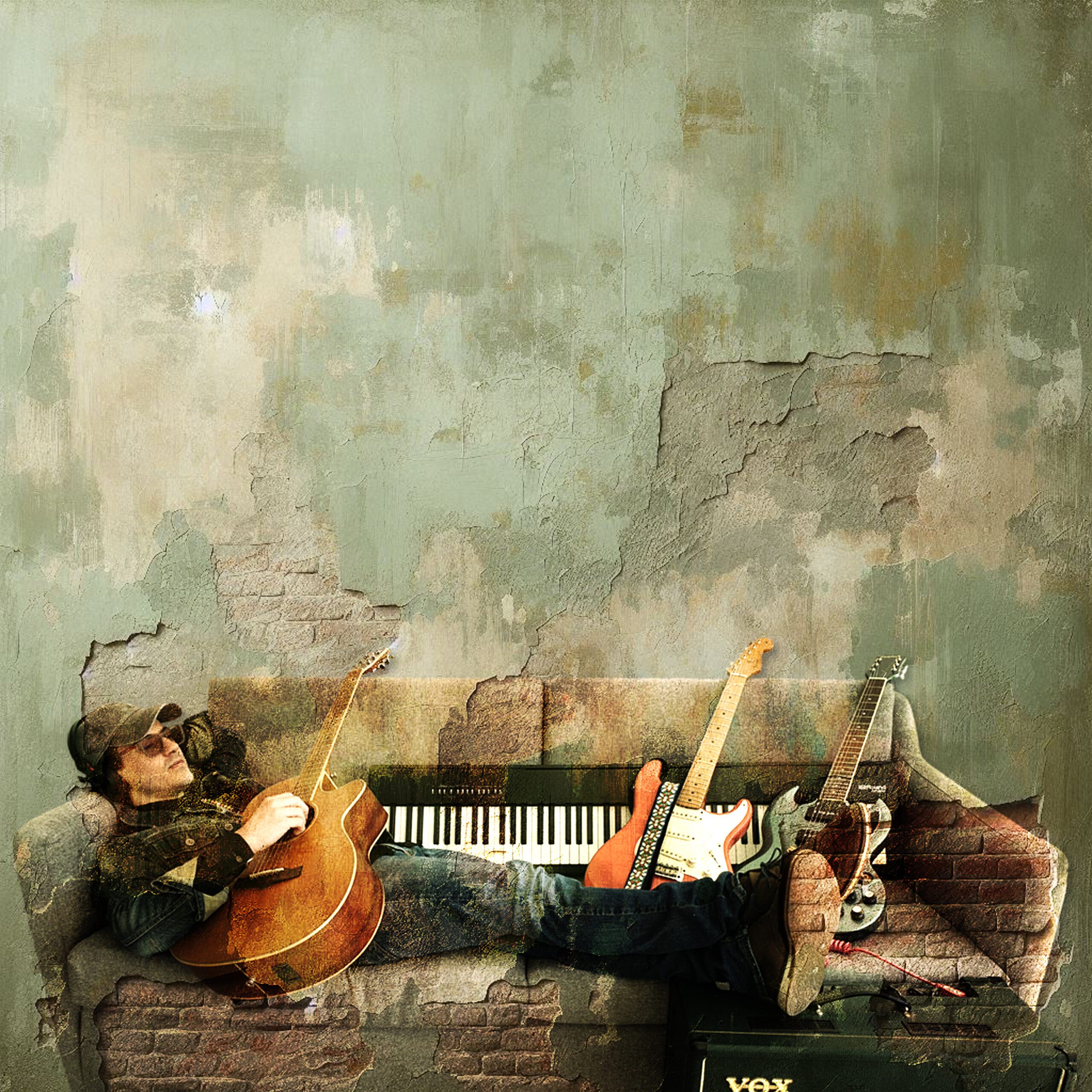 Jac Zamar lying on a worn couch surrounded by guitars and a keyboard against a textured wall
